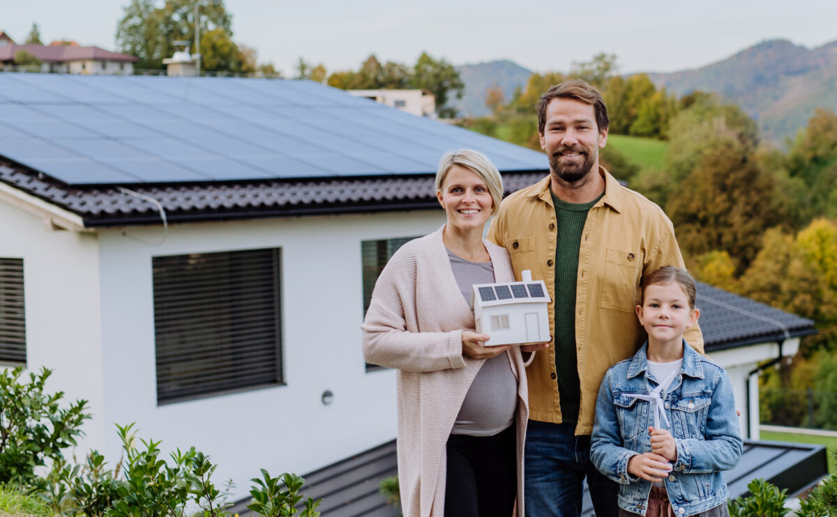 Familie vor ihrem Einfamilienhaus mit Solaranlage auf dem Dach