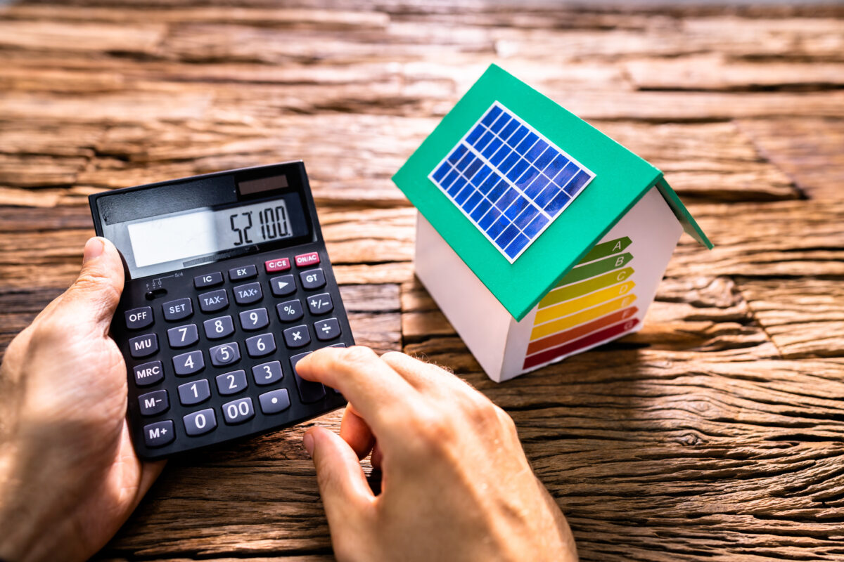 Taschenrechner neben einem Hausmodell mit Solarmodulen auf dem Dach